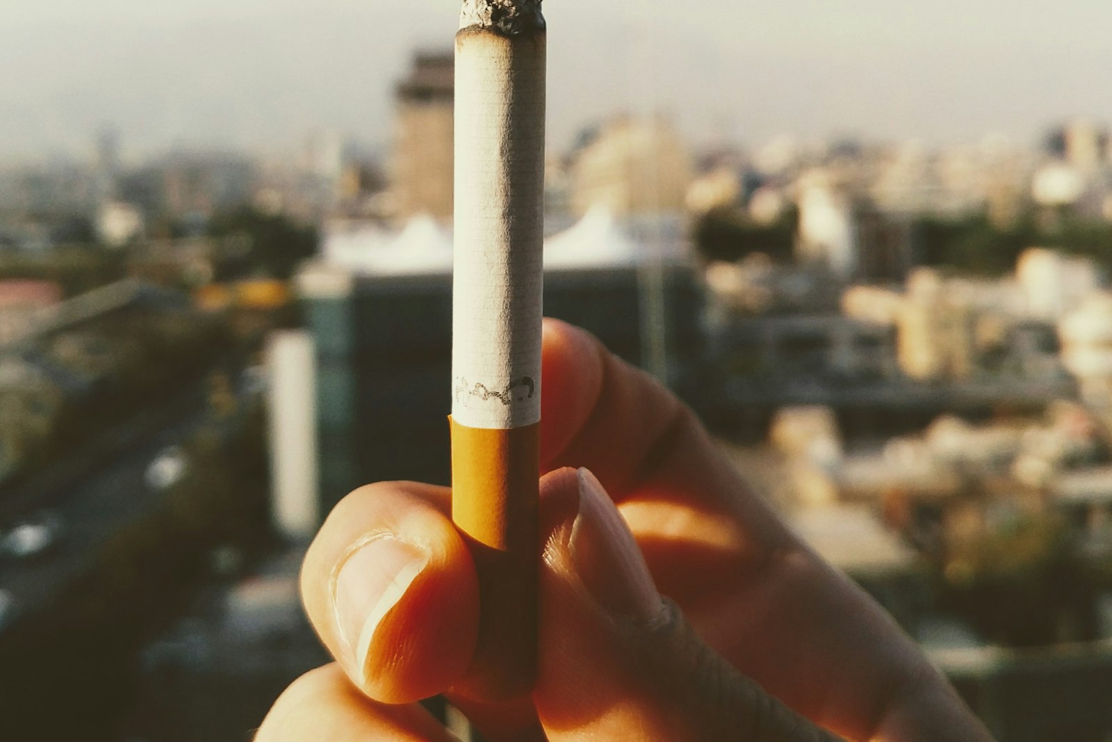 A cigarette held at a window above the city