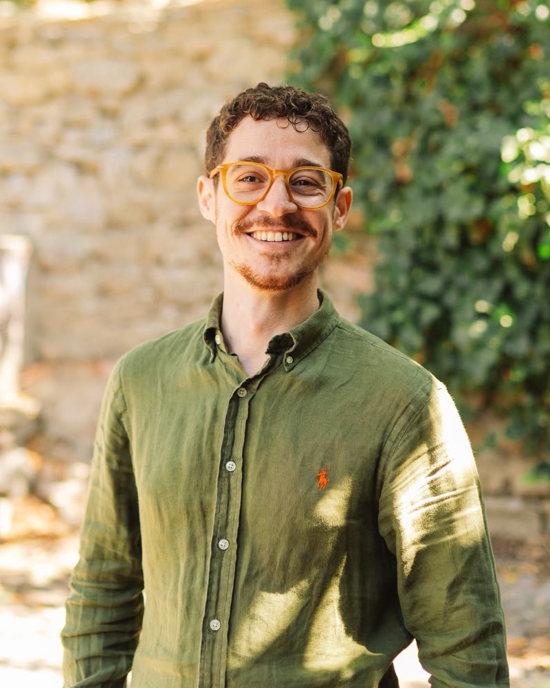 Osman Cemre Özerman, smiling, photographed in a garden beside a stone wall